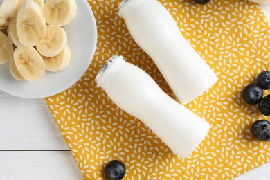 Photo of Tasty yogurt in bottles, banana and blueberries on white wooden table, top view
