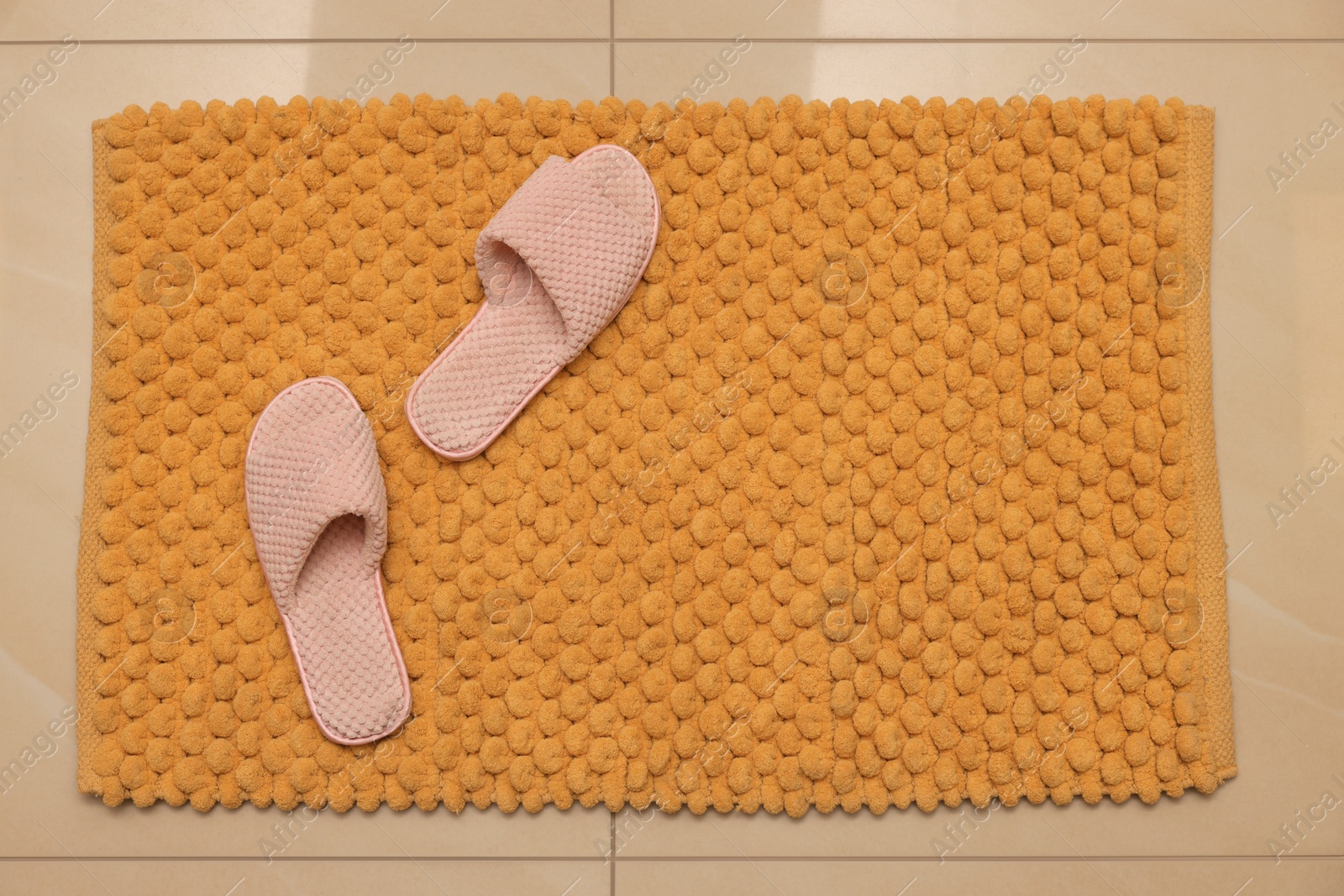 Photo of Soft orange bath mat and slippers on floor, top view