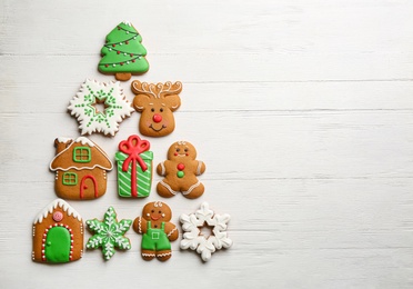 Photo of Christmas tree shape made of delicious gingerbread cookies on white wooden table, flat lay. Space for text