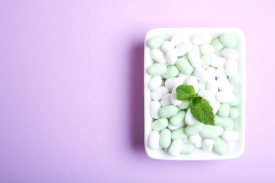 Photo of Plate with tasty mint candies and leaves on color background, top view