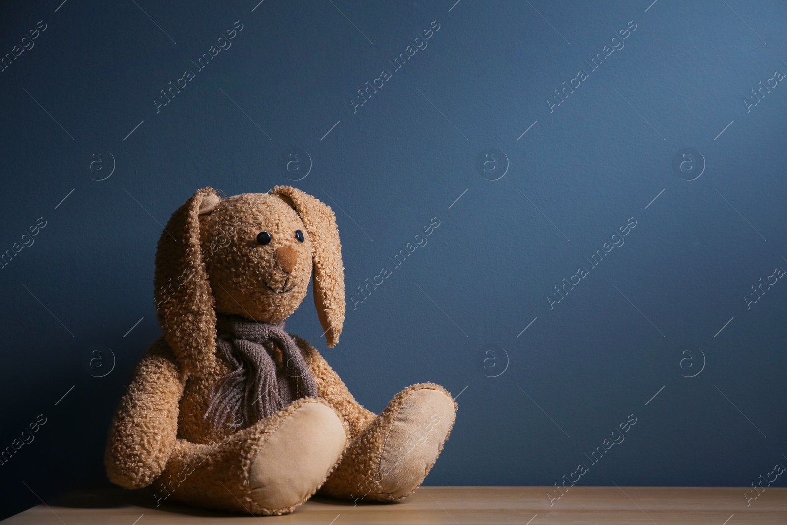 Photo of Abandoned toy bunny on table against dark background. Time to visit child psychologist