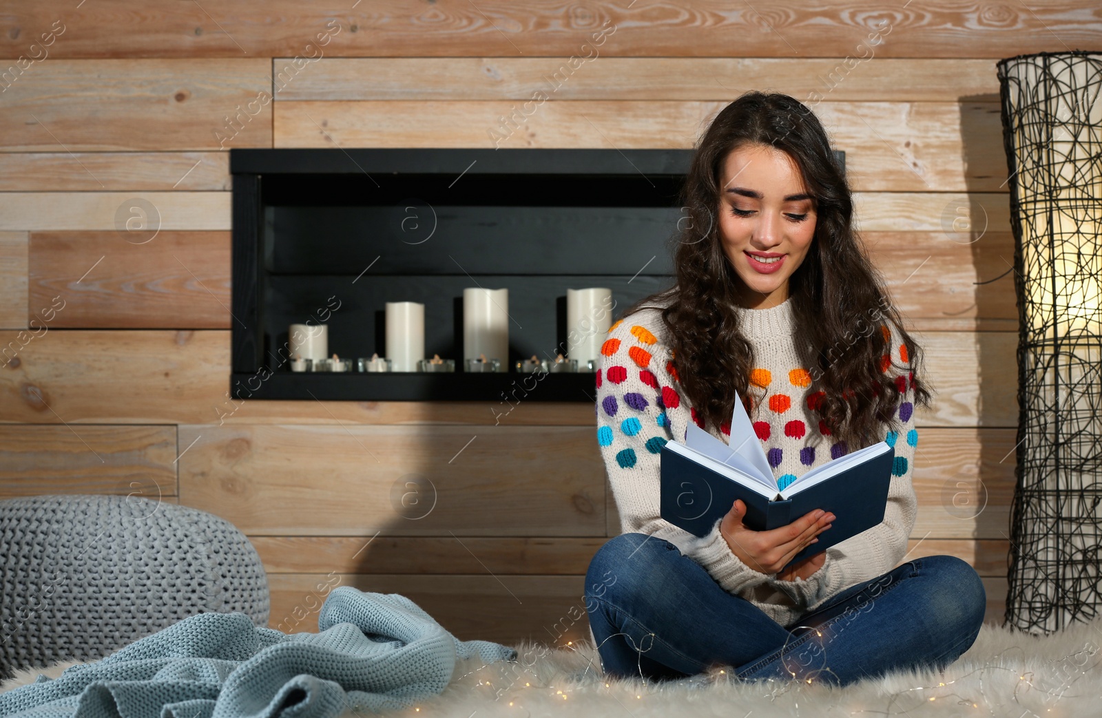 Photo of Young beautiful woman in warm sweater reading book on rug at home