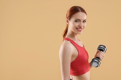 Photo of Young woman in sportswear doing exercises with dumbbell on beige background, space for text