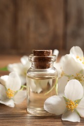 Photo of Jasmine essential oil and fresh flowers on wooden table