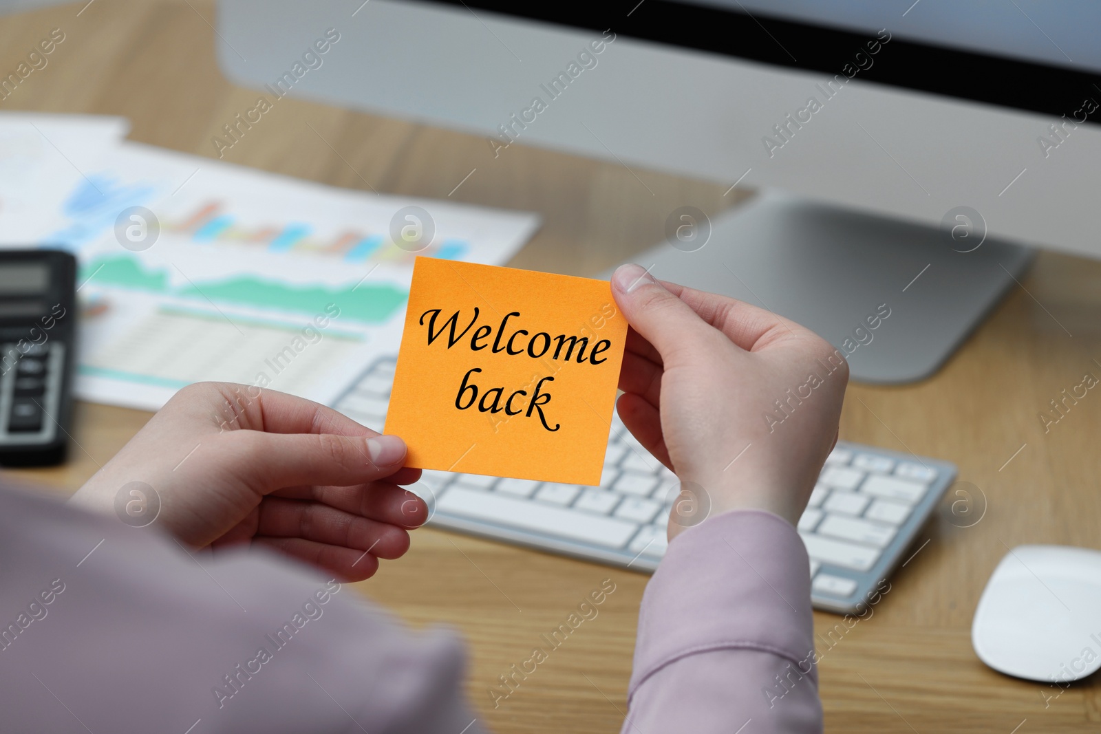 Image of Woman holding paper note with phrase Welcome Back at office desk, closeup