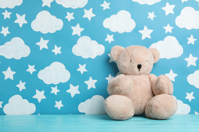 Photo of Teddy bear on wooden table near wall with painted blue sky, space for text. Baby room interior