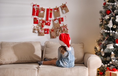 Cute little girl on sofa near Christmas advent calendar at home