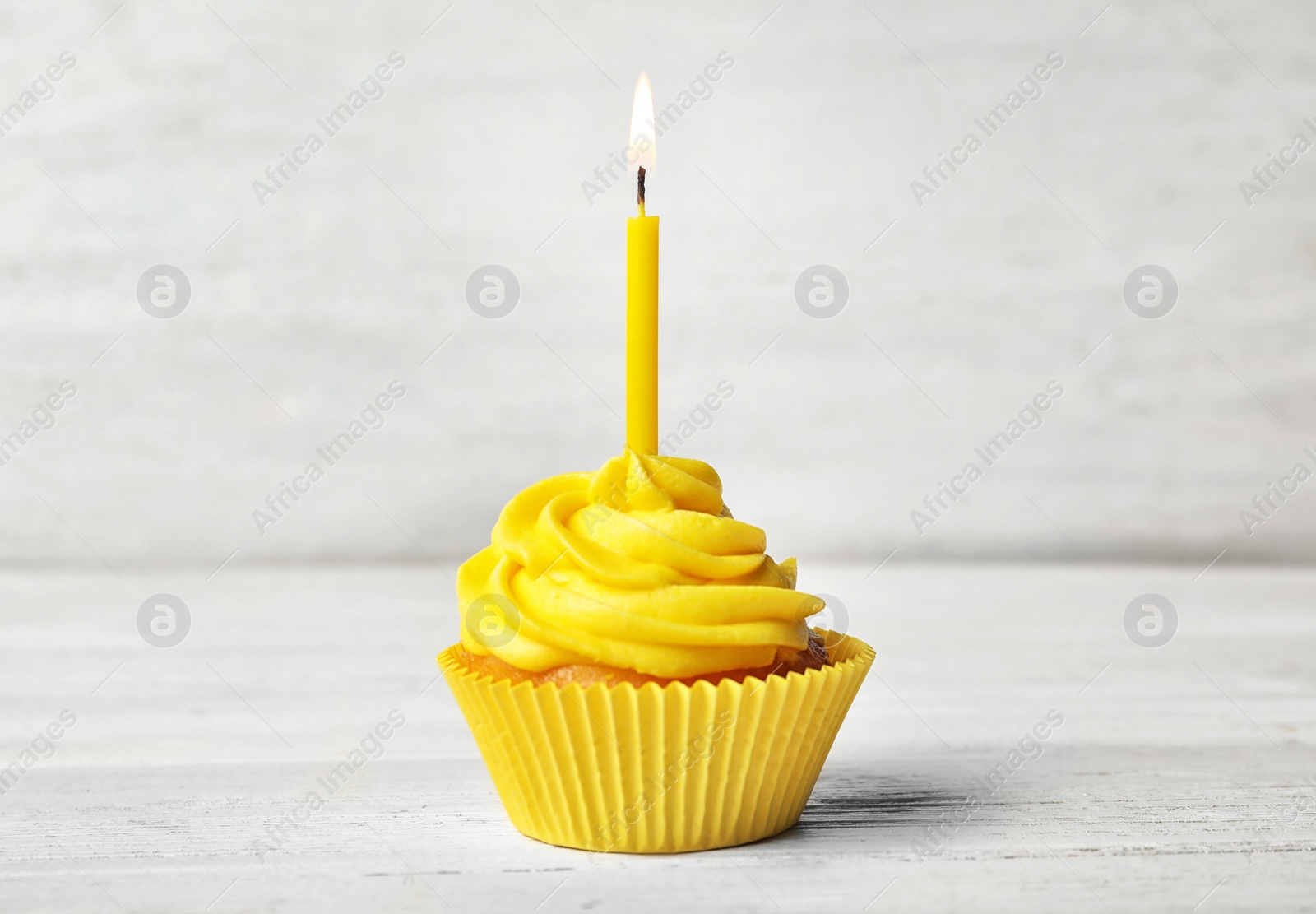 Photo of Delicious birthday cupcake with cream and burning candle on white wooden table