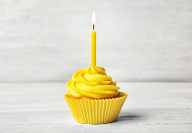 Delicious birthday cupcake with cream and burning candle on white wooden table