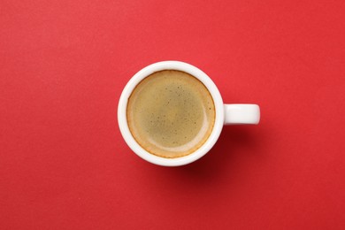 Aromatic coffee in cup on red background, top view