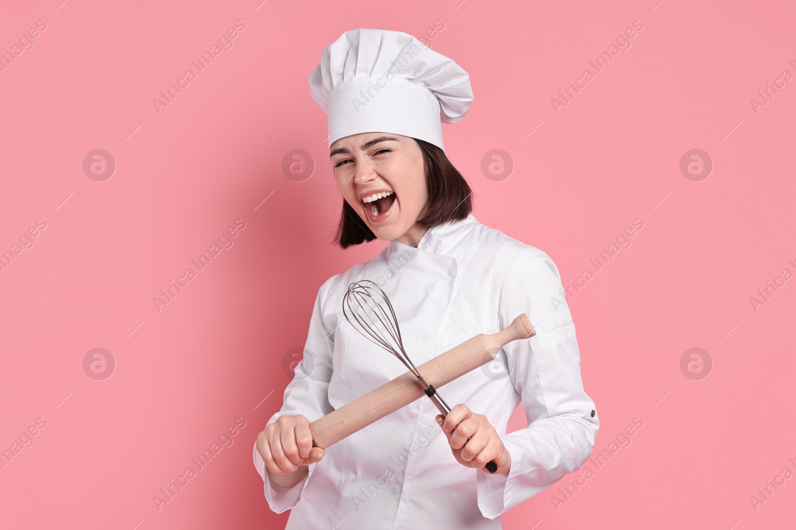 Photo of Happy confectioner with rolling pin and whisk on pink background