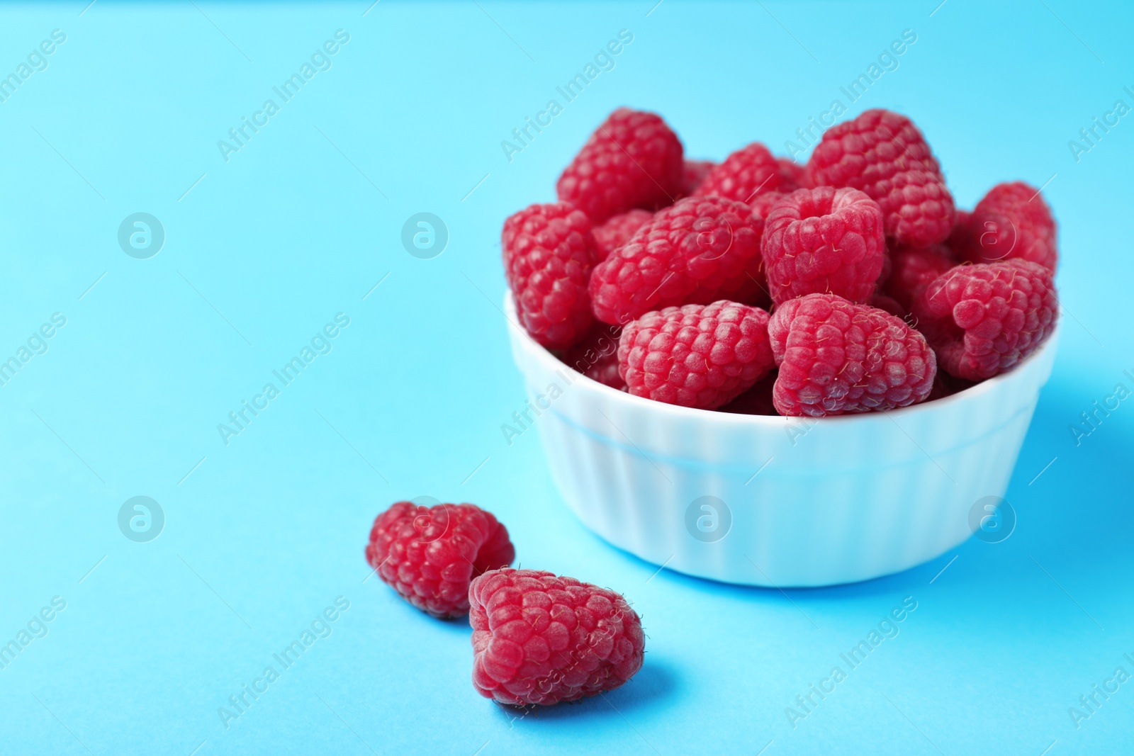 Photo of Bowl of delicious ripe raspberries on blue background. Space for text