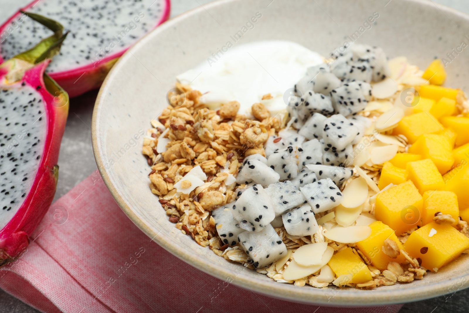 Photo of Bowl of granola with pitahaya, mango and yogurt on table, closeup