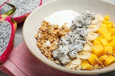 Photo of Bowl of granola with pitahaya, mango and yogurt on table, closeup