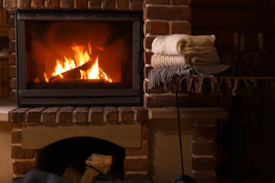 Photo of Stack of knitwear near fireplace with burning wood indoors. Winter vacation