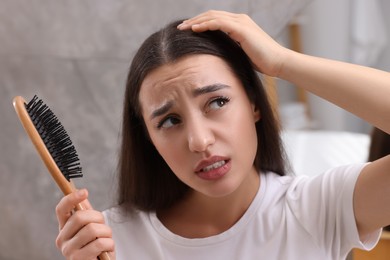 Photo of Emotional woman with brush examining her hair at home. Dandruff problem