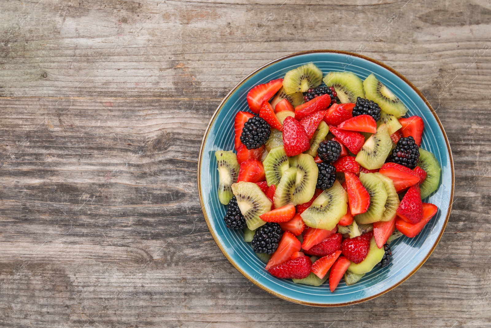 Photo of Plate of delicious fresh fruit salad on wooden table, top view. Space for text
