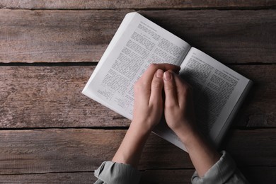 Photo of Religion. Christian woman praying over Bible at wooden table, top view. Space for text