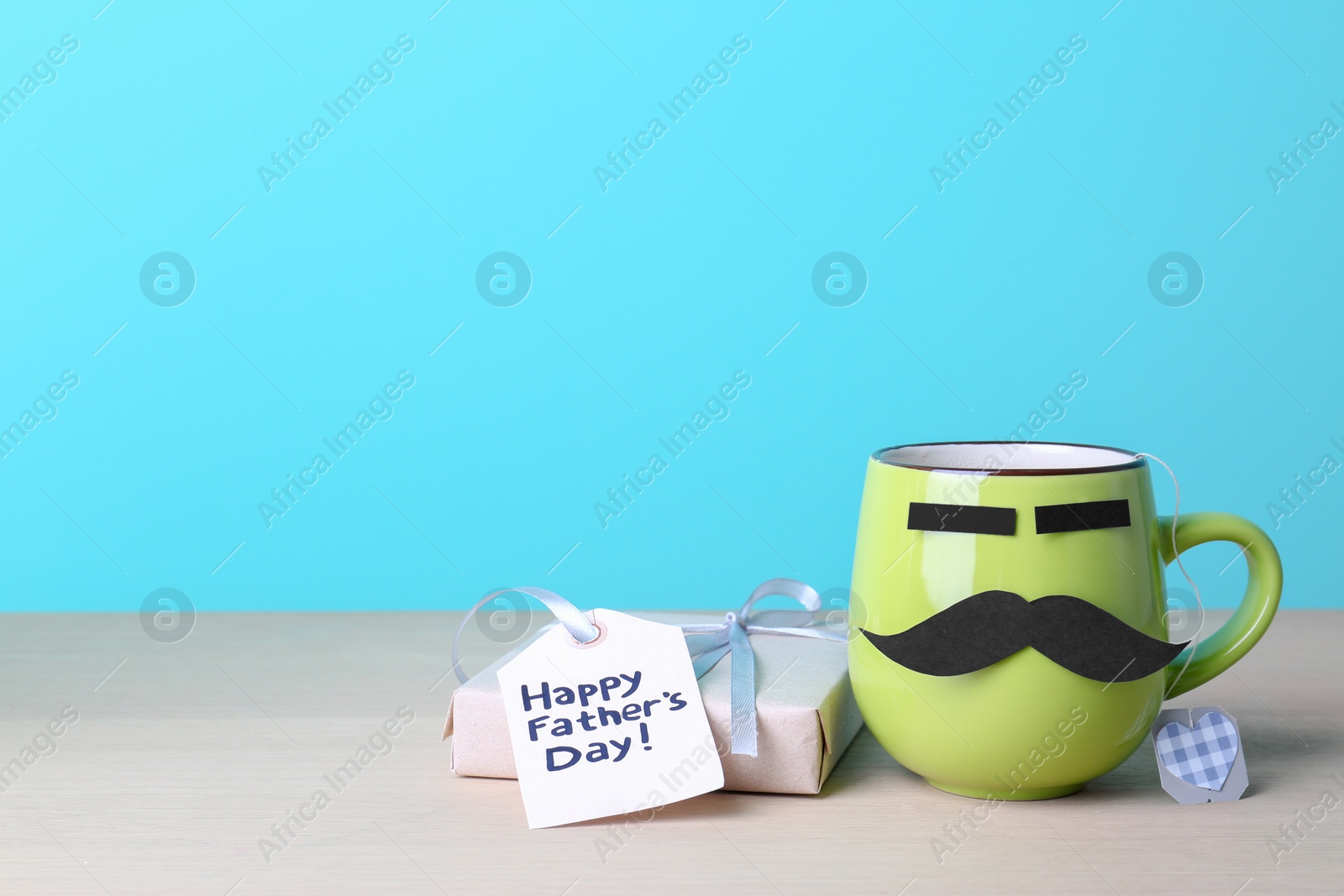 Photo of Cup with mustache and gift box on table against color background. Father's day celebration