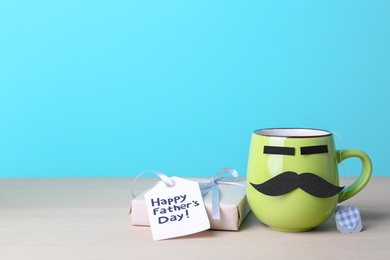 Cup with mustache and gift box on table against color background. Father's day celebration