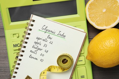 Photo of Notebook with products of low glycemic index, calculator, measuring tape and lemons on wooden table, top view