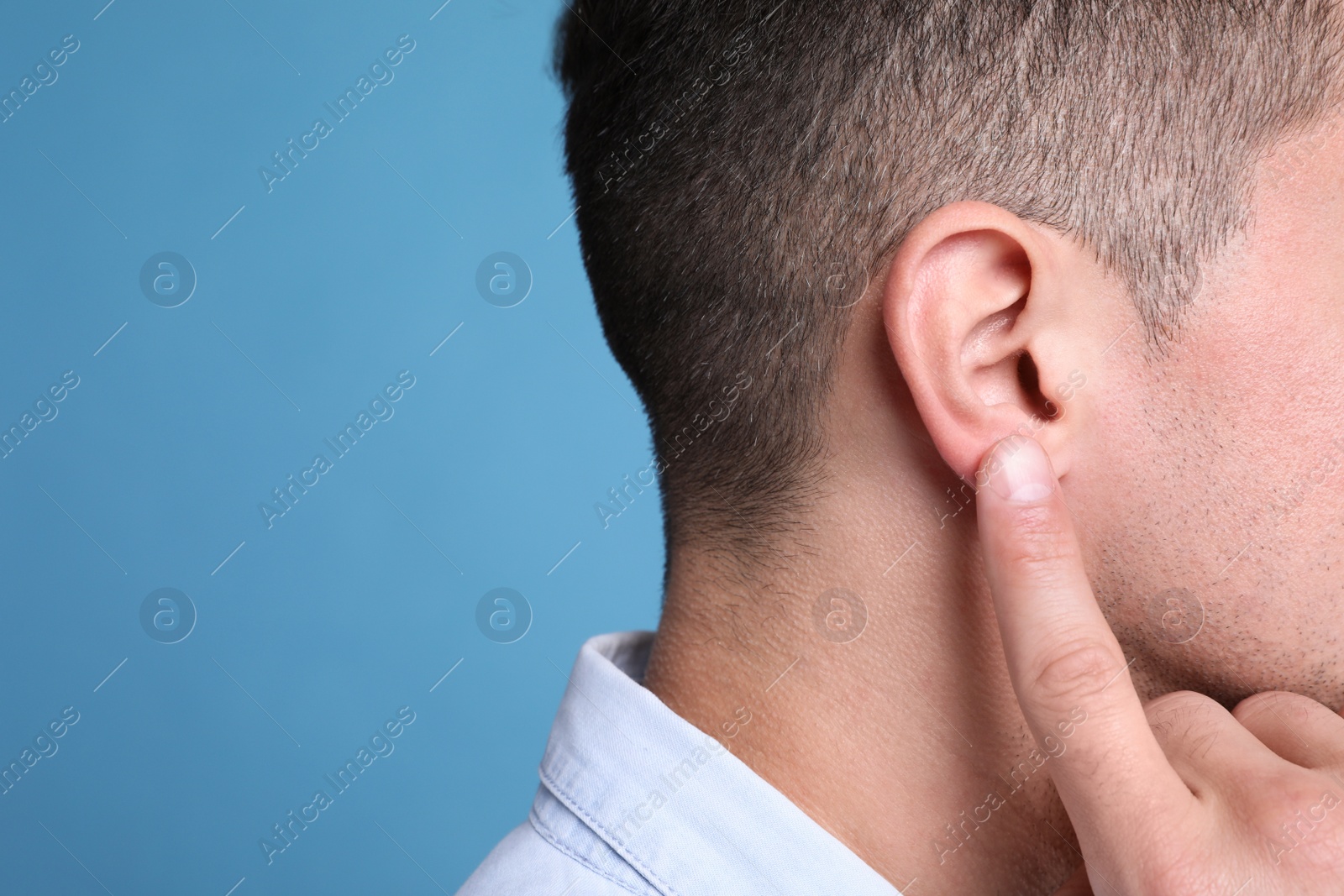 Photo of Man pointing at his ear on light blue background, closeup. Space for text