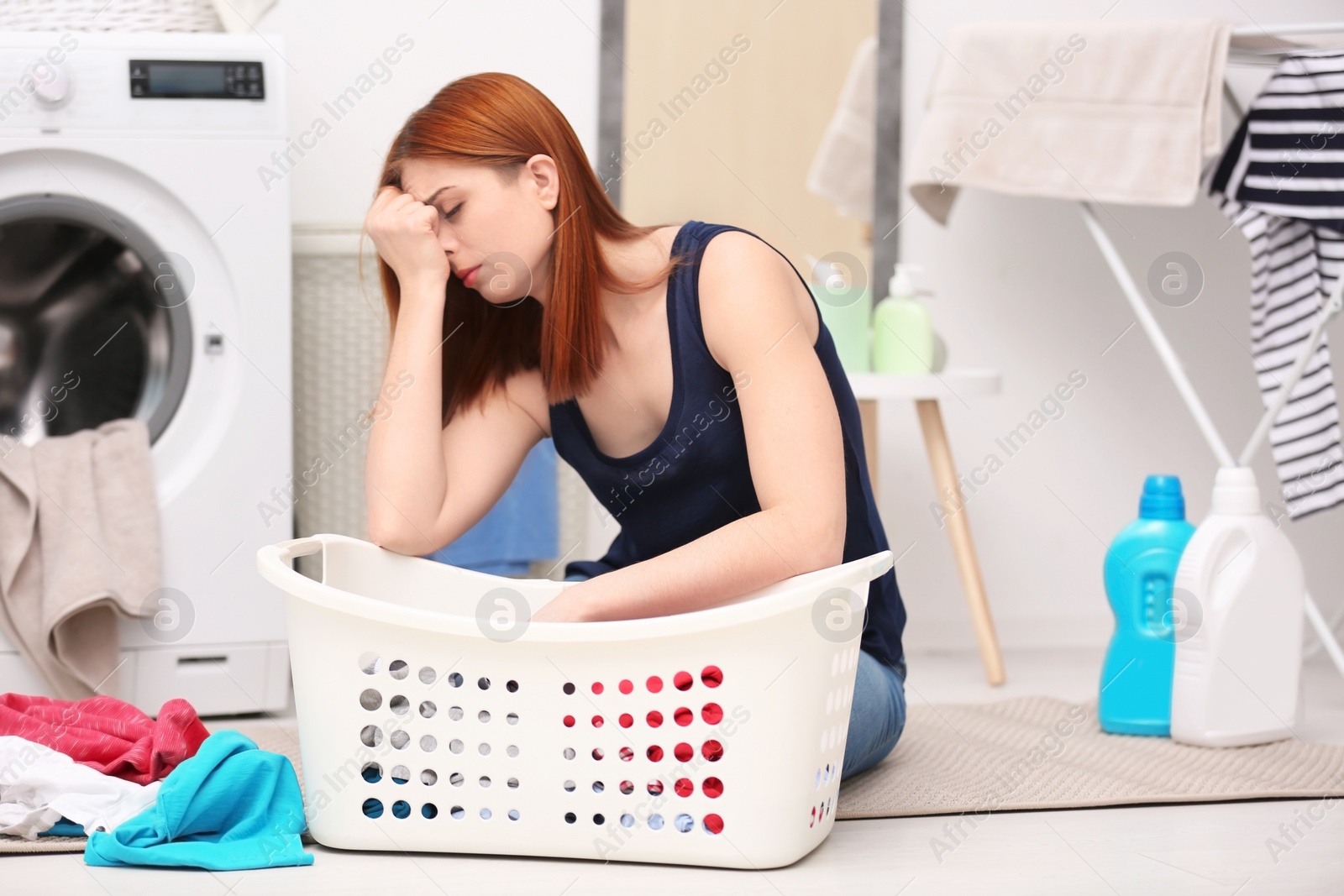 Photo of Tired housewife with basket of clothes in laundry room