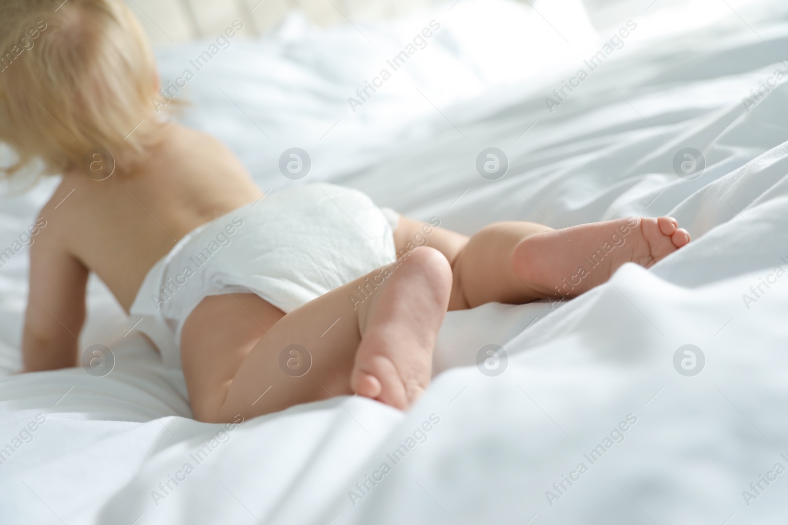 Photo of Cute little baby in diaper in bedroom, focus on legs