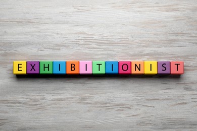 Photo of Word EXHIBITIONIST made with colorful cubes on white wooden table, flat lay