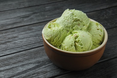 Photo of Delicious green ice cream served in ceramic bowl on wooden table