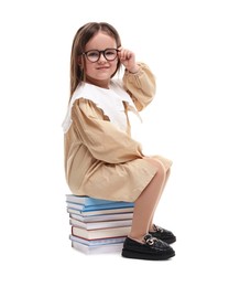 Photo of Cute little girl in glasses sitting on stack of books against white background