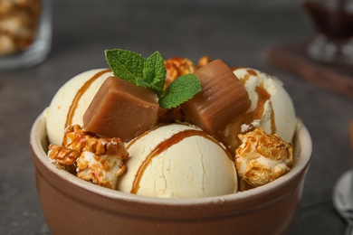 Photo of Delicious ice cream with caramel and popcorn in bowl on table, closeup