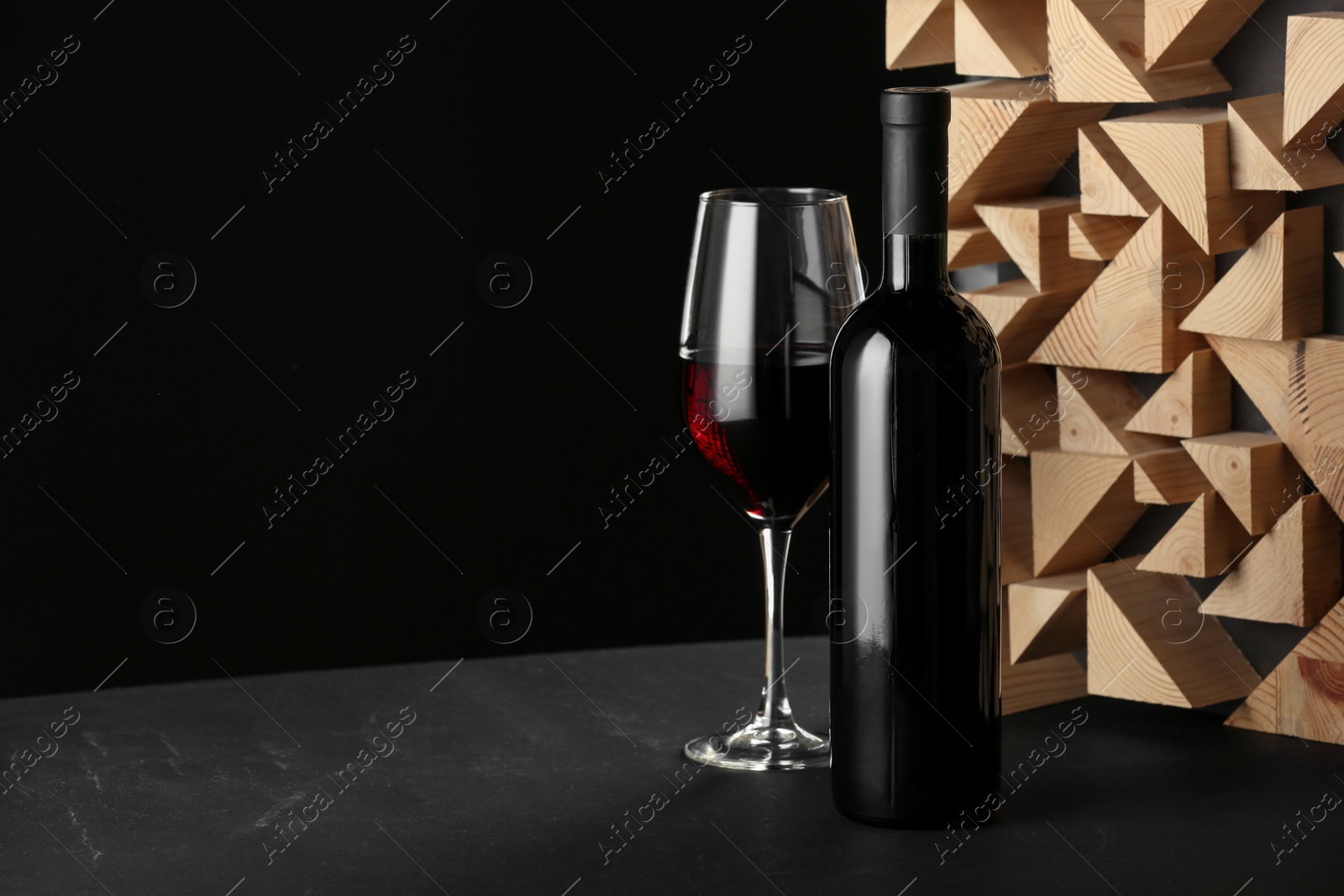 Photo of Stylish presentation of red wine in bottle and wineglass on table against black background, space for text