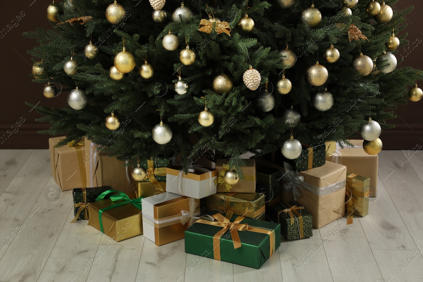 Photo of Beautifully decorated Christmas tree and many gift boxes near brown wall indoors, closeup