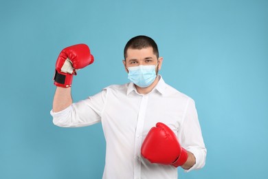 Photo of Man with protective mask and boxing gloves on light blue background. Strong immunity concept