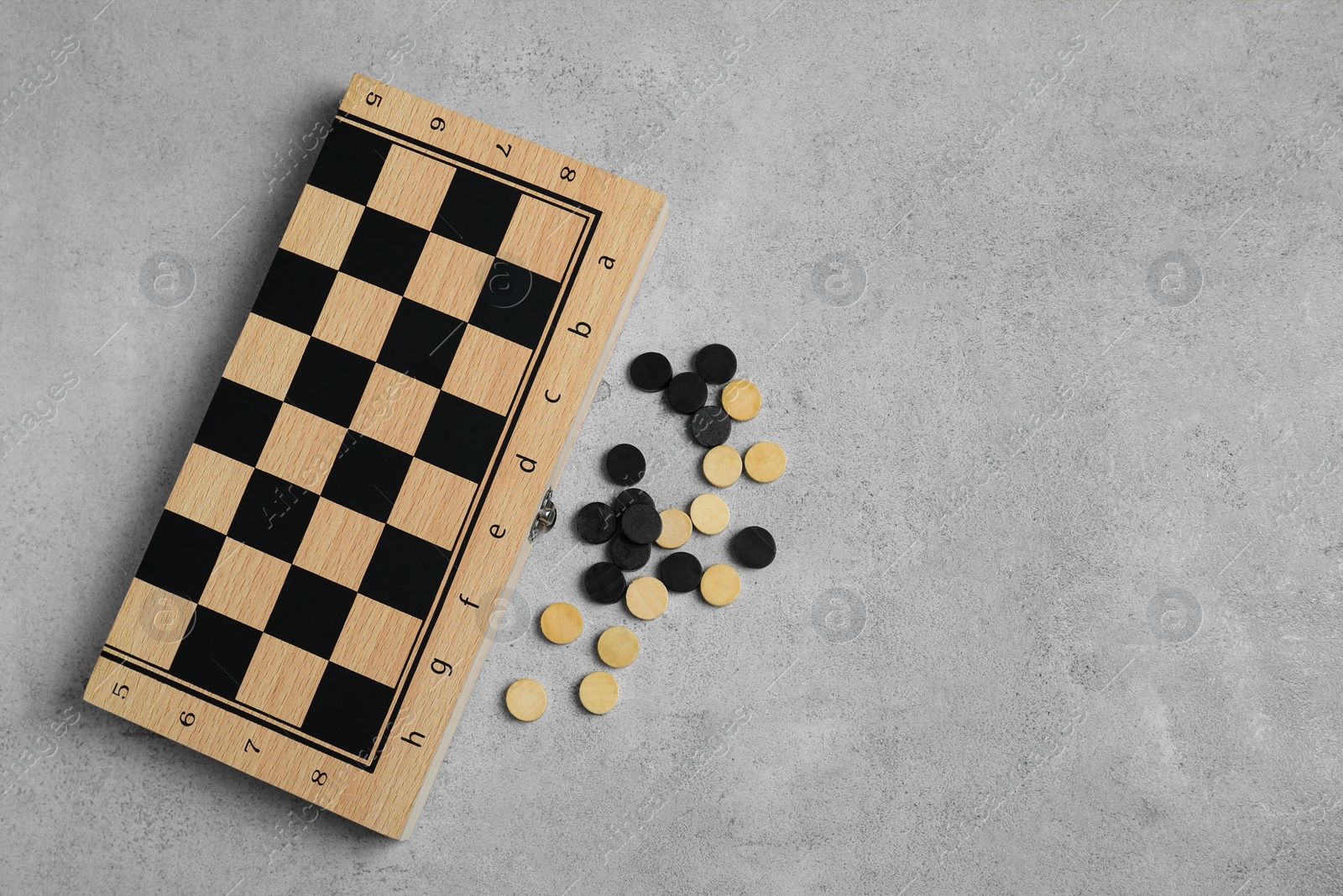 Photo of Wooden checkerboard and game pieces on light grey table, flat lay. Space for text