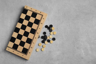 Wooden checkerboard and game pieces on light grey table, flat lay. Space for text