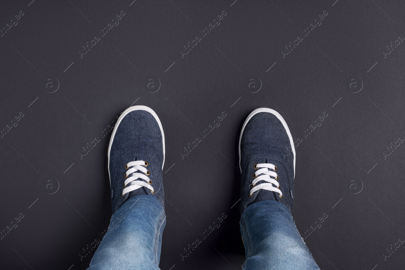 Photo of Child in stylish sneakers standing on black background, top view