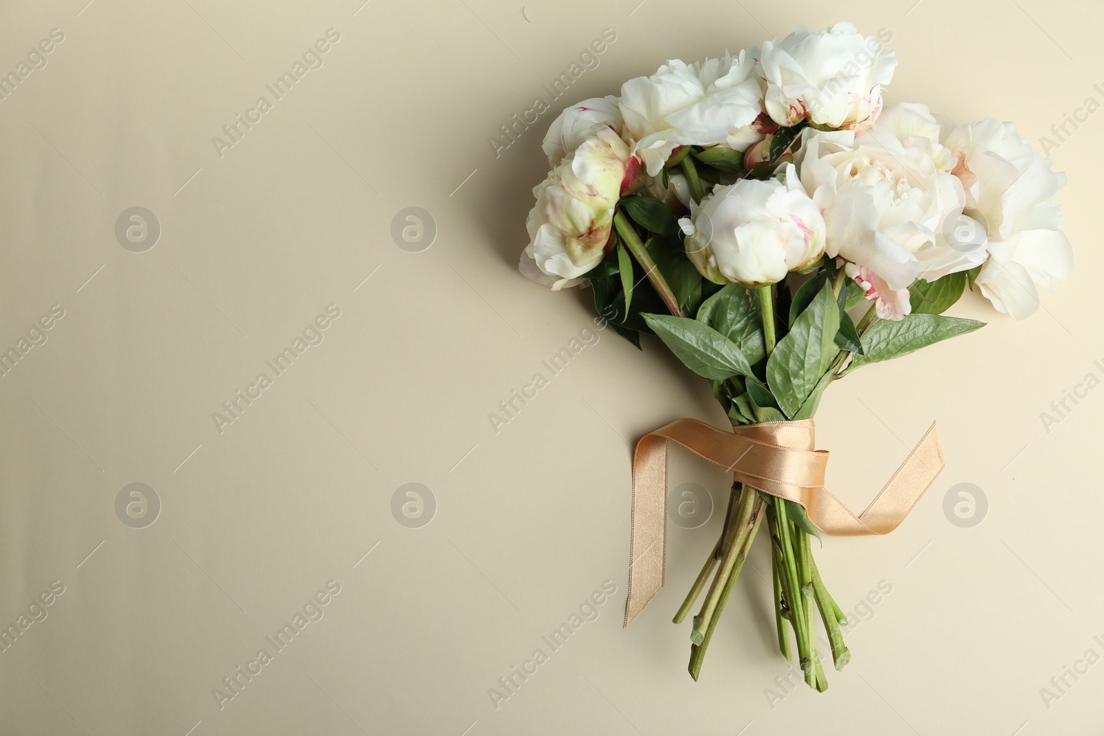 Photo of Bouquet of beautiful peonies with ribbon on beige background, flat lay. Space for text