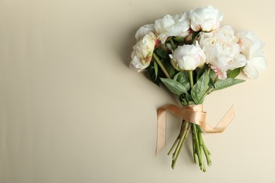 Bouquet of beautiful peonies with ribbon on beige background, flat lay. Space for text