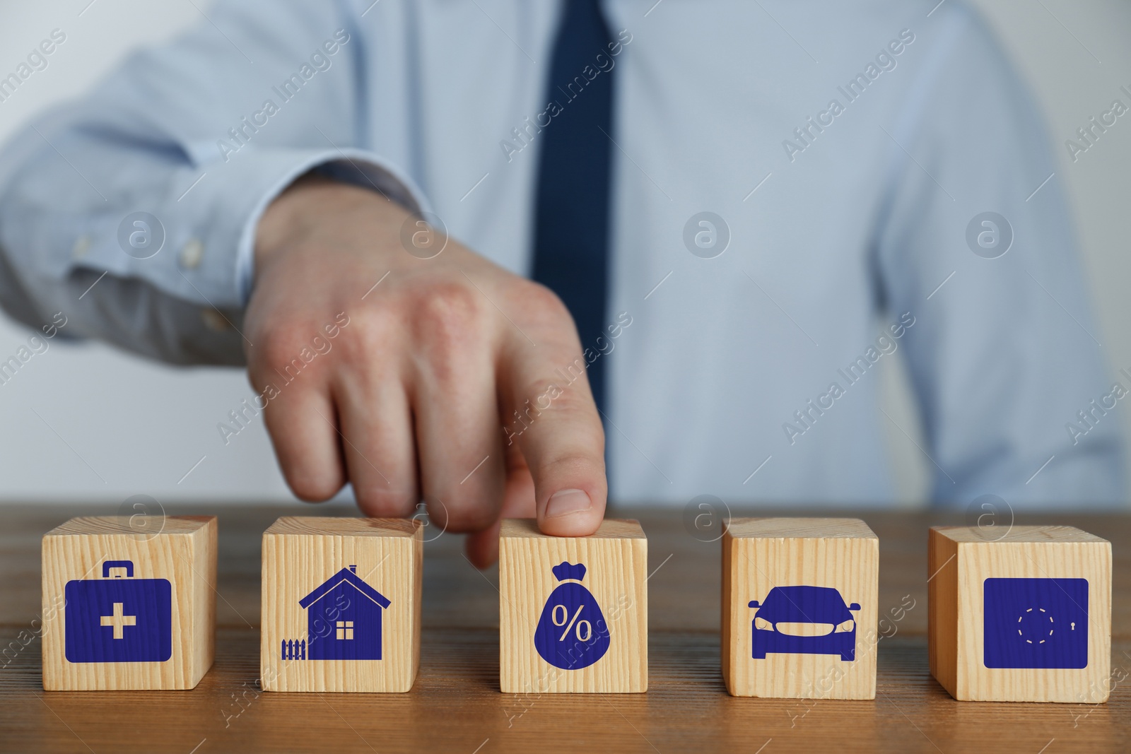 Image of Man and wooden cubes with different icons on wooden table, closeup. Insurance concept