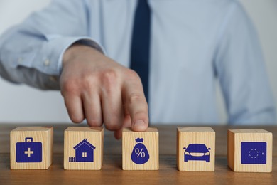 Man and wooden cubes with different icons on wooden table, closeup. Insurance concept