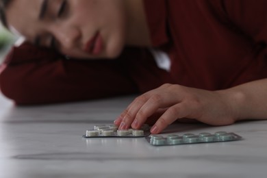 Photo of Woman with antidepressant pills sleeping at white marble table, selective focus
