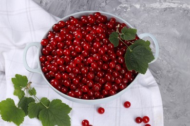 Photo of Ripe red currants and leaves in colander on grey textured table, above view