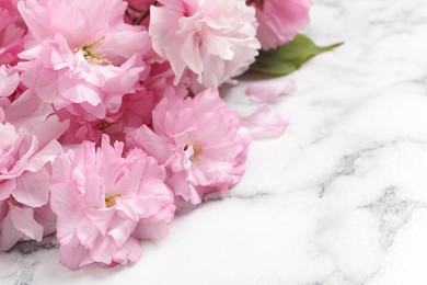 Photo of Beautiful sakura tree blossoms on white marble table, closeup. Space for text
