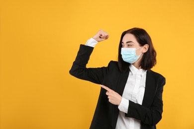 Photo of Businesswoman with protective mask showing muscles on yellow background, space for text. Strong immunity concept