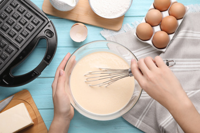 Woman preparing dough for Belgian waffles at light blue wooden table, top view