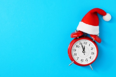 Photo of Alarm clock in Santa hat on light blue background, top view with space for text. New Year countdown