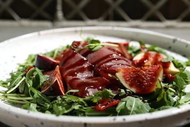 Plate of tasty bresaola salad with figs, sun-dried tomatoes and balsamic vinegar on table, closeup
