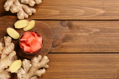 Photo of Spicy pickled ginger and root on wooden table, flat lay. Space for text